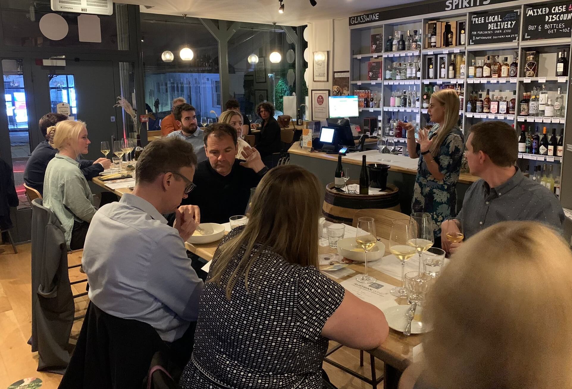 Picture of a wine tasting in The Good Wine Shop Richmond store with people seating around tables with charcuterie and cheese, listening to the host talking about the wines they are tasting